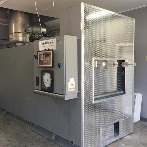 A large, industrial Matthews cremation unit with a grey control panel and a diamond-plate metal front door.