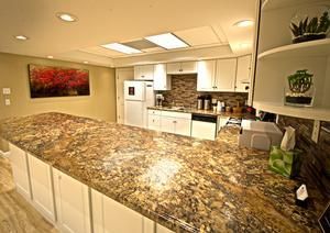 A kitchen with a large granite island, white cabinets, stainless steel appliances, and a red landscape painting on the wall.