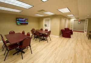 A dining room with maroon tables and chairs, a television on the wall, and red armchairs in a seating area.