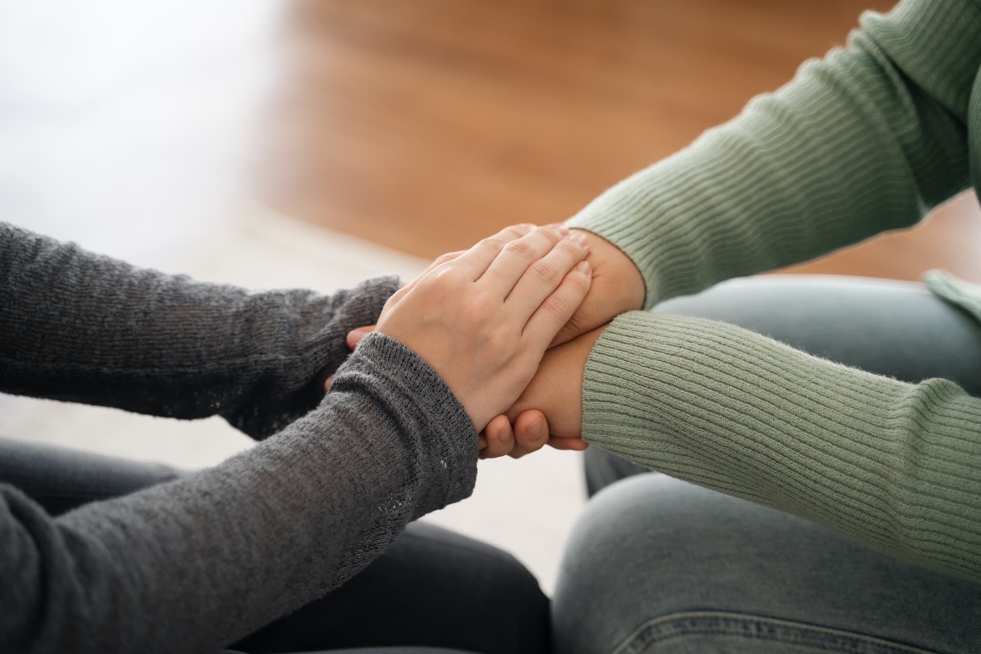 Two people sitting together, one gently holding the other's hands in a gesture of support and comfort.
