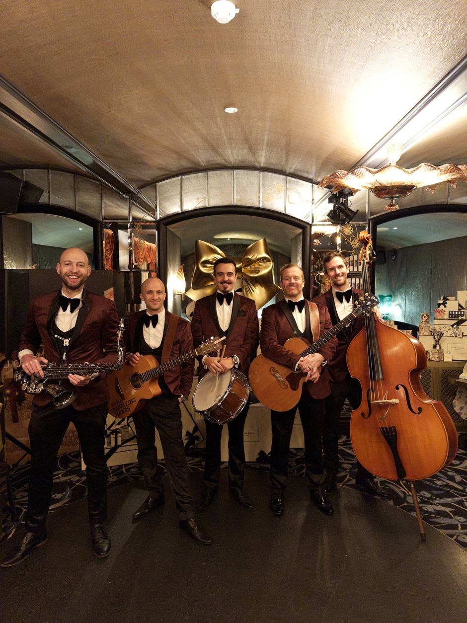 String quartet and double bass ensemble standing in a hallway, holding instruments under warm lights.