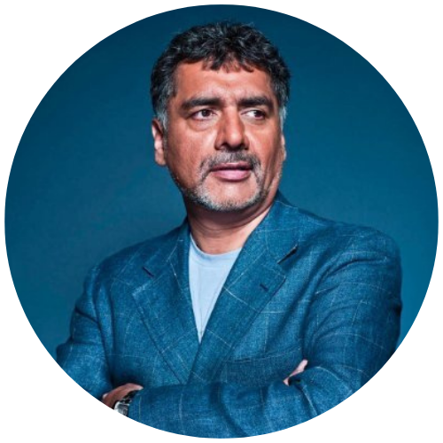 Portrait of a man in a blue blazer against a teal background, looking to the side with arms crossed