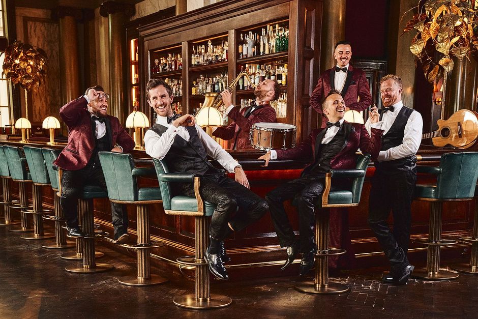 Group of people in a warmly lit bar, posing with drinks and smiling at the counter.