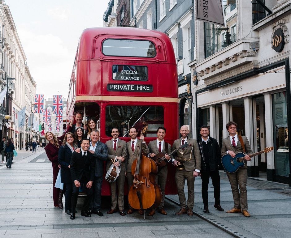 Street band posing in front of a red double-decker bus on a city street