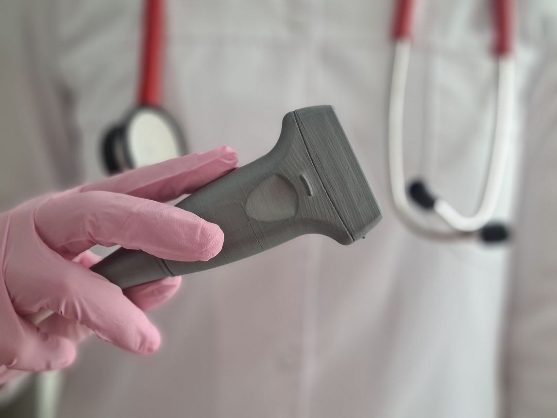 Un médico que lleva guantes rosas sostiene una máquina de ultrasonido frente a un estetoscopio.