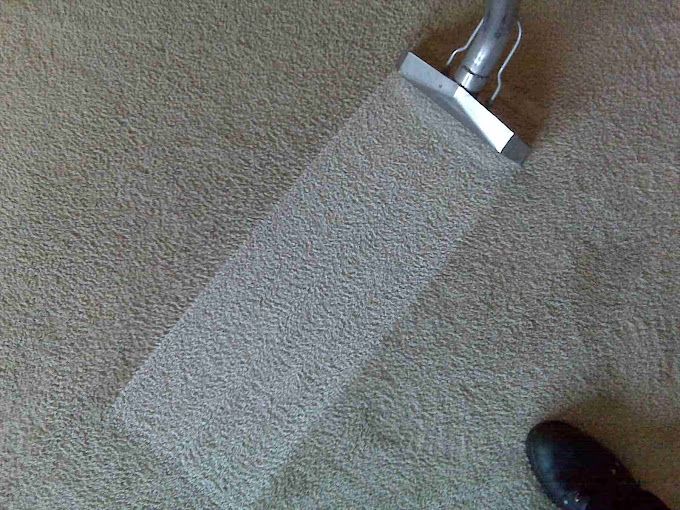 A person is cleaning a carpet with a vacuum cleaner.