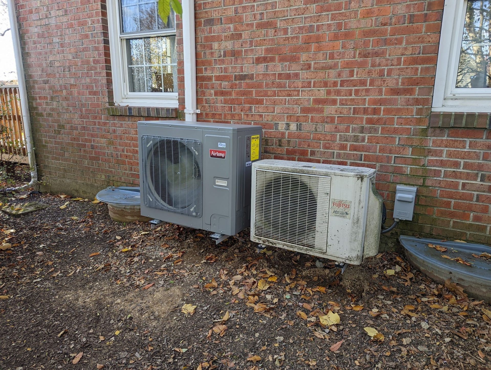 Two air conditioners are sitting on the side of a brick building.
