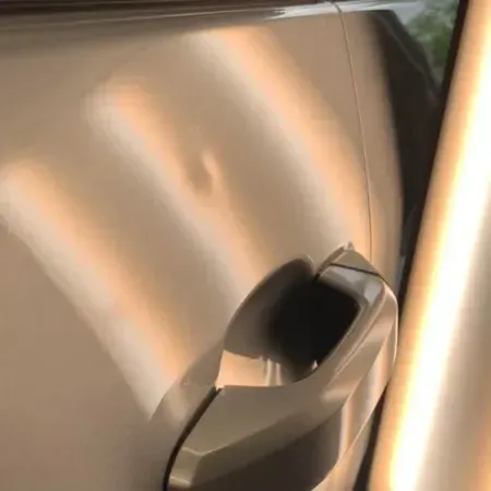 Close-up of a silver car’s door handle on a metallic beige vehicle.