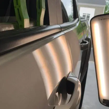 Close-up of a silver car door handle and side mirror reflecting a garage