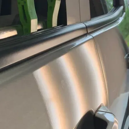 Close-up of a silver car door and black roof rail, with a faint orange reflection.