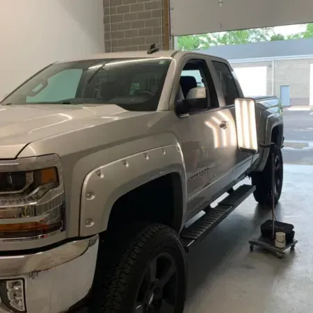 Silver pickup truck in a garage, lifted with a jack near the front wheel