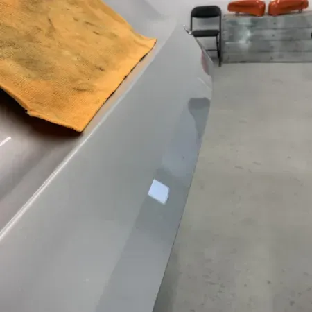 Gray car panel in a garage, partially covered by a yellow cloth with a white tape square on the side