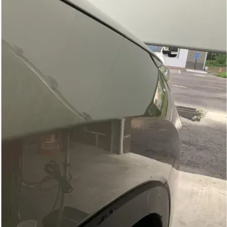 Close-up of a white car’s front fender and headlight in a driveway under a carport.