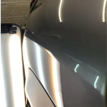 Close-up of a silver car beside a white vehicle in a garage, with bright reflections on the body panels