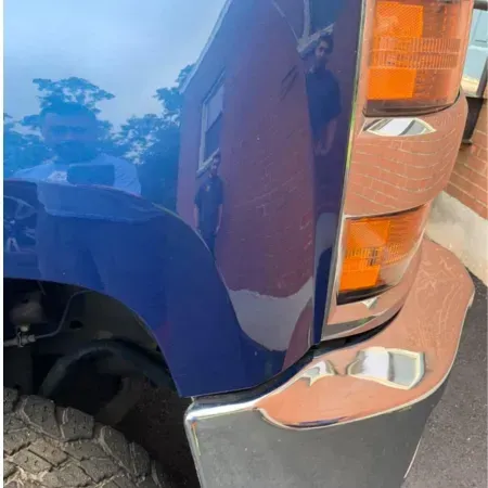 Close-up of a blue truck’s front fender and chrome bumper on a paved road
