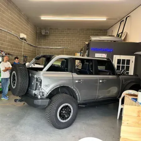 Gray off-road SUV in a garage, lifted with large tires and a spare mounted on the back.