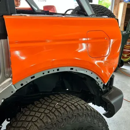 Orange off-road vehicle body panel above a large tire, with exposed wheel arch in a garage