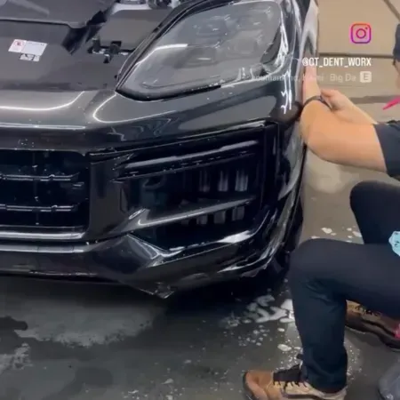 Worker polishing the front of a black sports car in a detailing shop