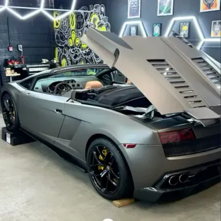 Silver Lamborghini convertible with rear engine cover open in a custom garage with neon wall art.