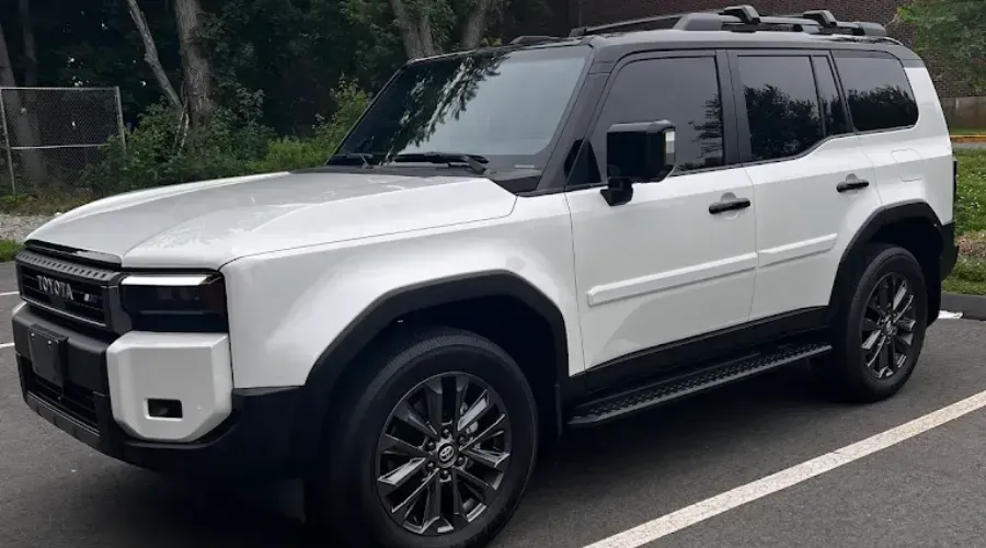White SUV parked on a street, front-left view, with roof rack and dark tinted windows