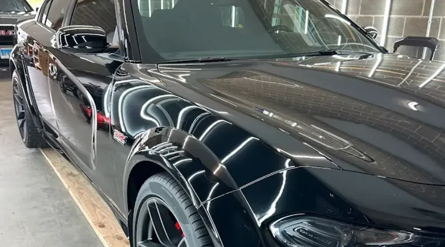 Black sports car parked indoors, close-up on the front side and hood with bright reflections.