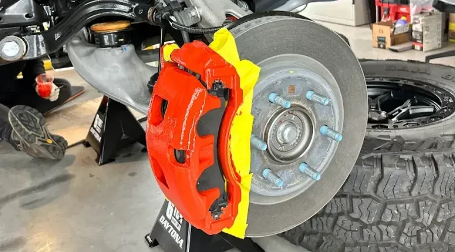 Close-up of a car brake rotor with a bright red and yellow brake caliper in a garage