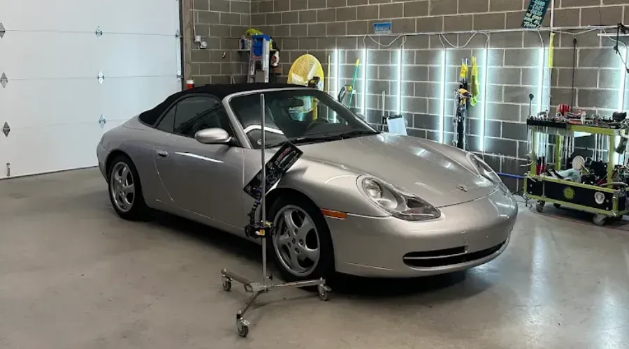 Silver sports car in a garage being inspected with a tripod-mounted camera rig.