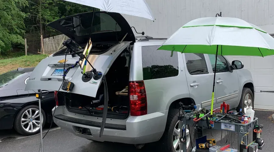 Silver SUV with open rear hatch and camping gear in a parking lot, with a green-and-white umbrella attached nearby