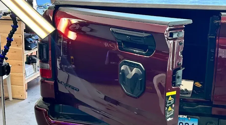 Dark red Ram pickup tailgate damaged, with the rear bed open in a garage or repair shop.
