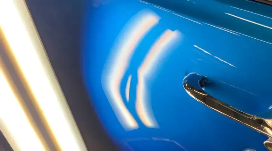 Close-up of a blue car body with bright white reflections and a chrome door handle