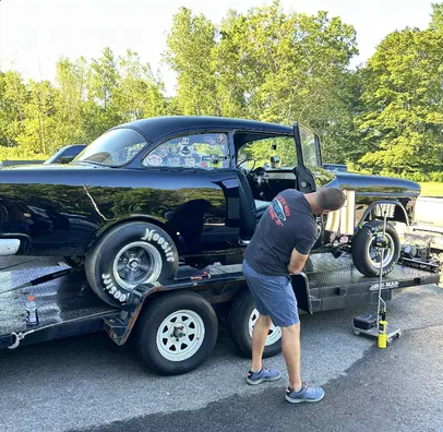 Man working on a black race car on a trailer in a sunny outdoor lot Man working on a black race car on a trailer in a sunny outdoor lot