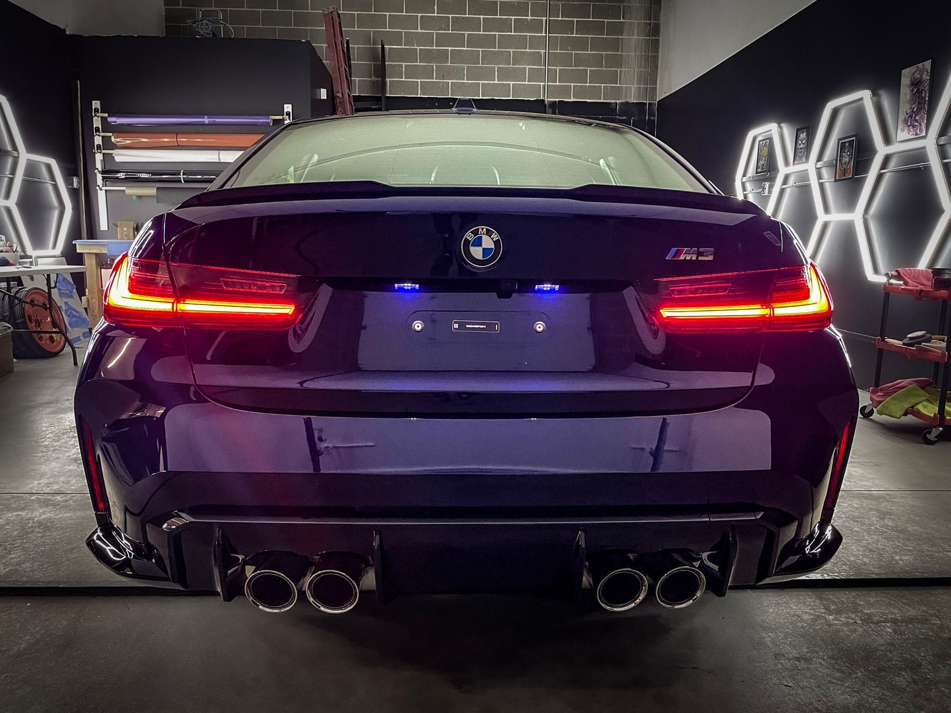 Rear view of a black BMW sedan with taillights on in a garage, showing quad exhausts.