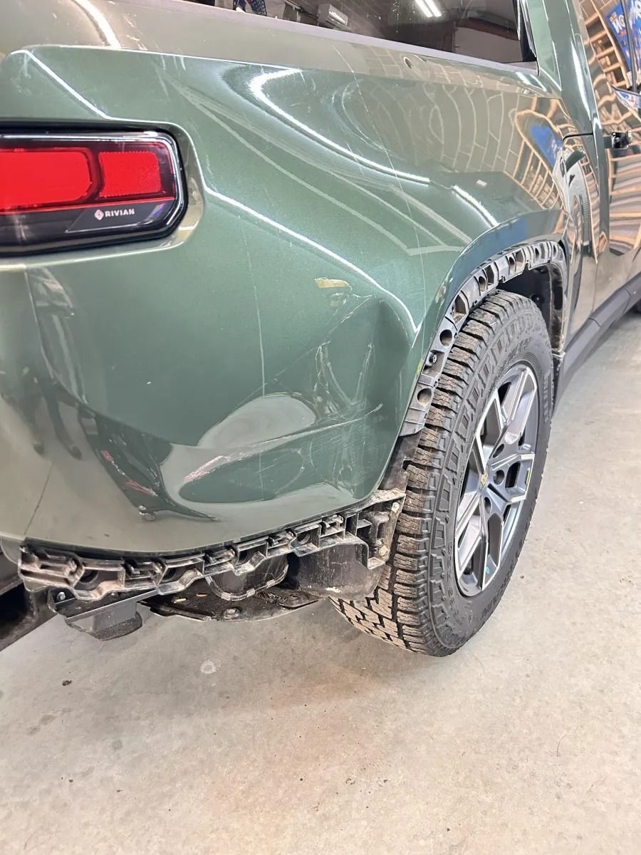 Damaged green SUV rear bumper and quarter panel in a repair shop