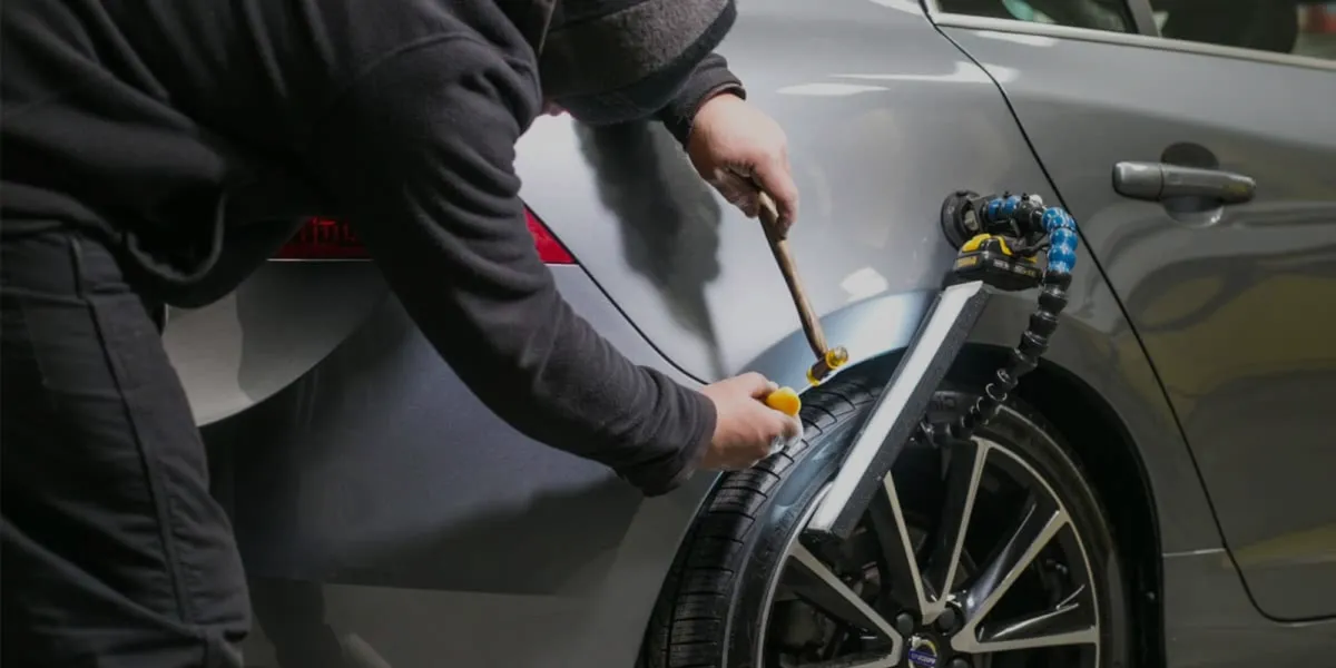 Person using a measuring tool on a gray car door panel near the front wheel