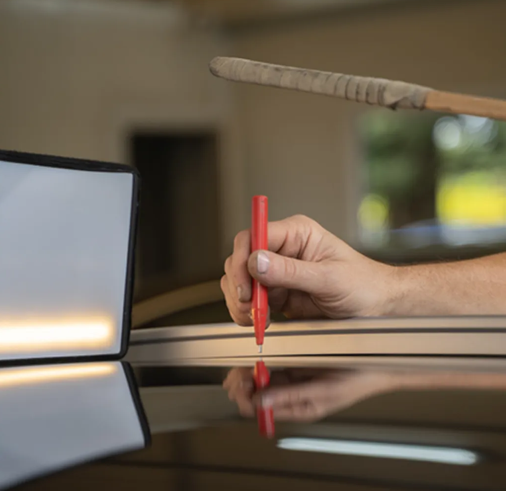Hand holding a red pen over a glossy table with a blurred laptop in the background Hand holding a red pen over a glossy table with a blurred laptop in the background