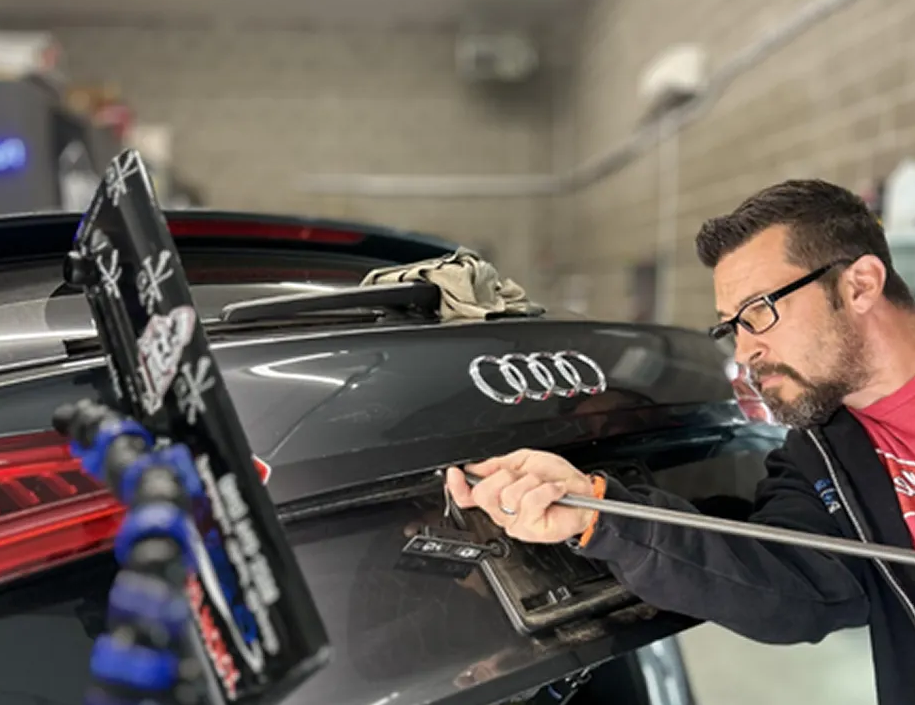 Technician polishing the rear of a black Audi in a garage, using a cloth and tool.