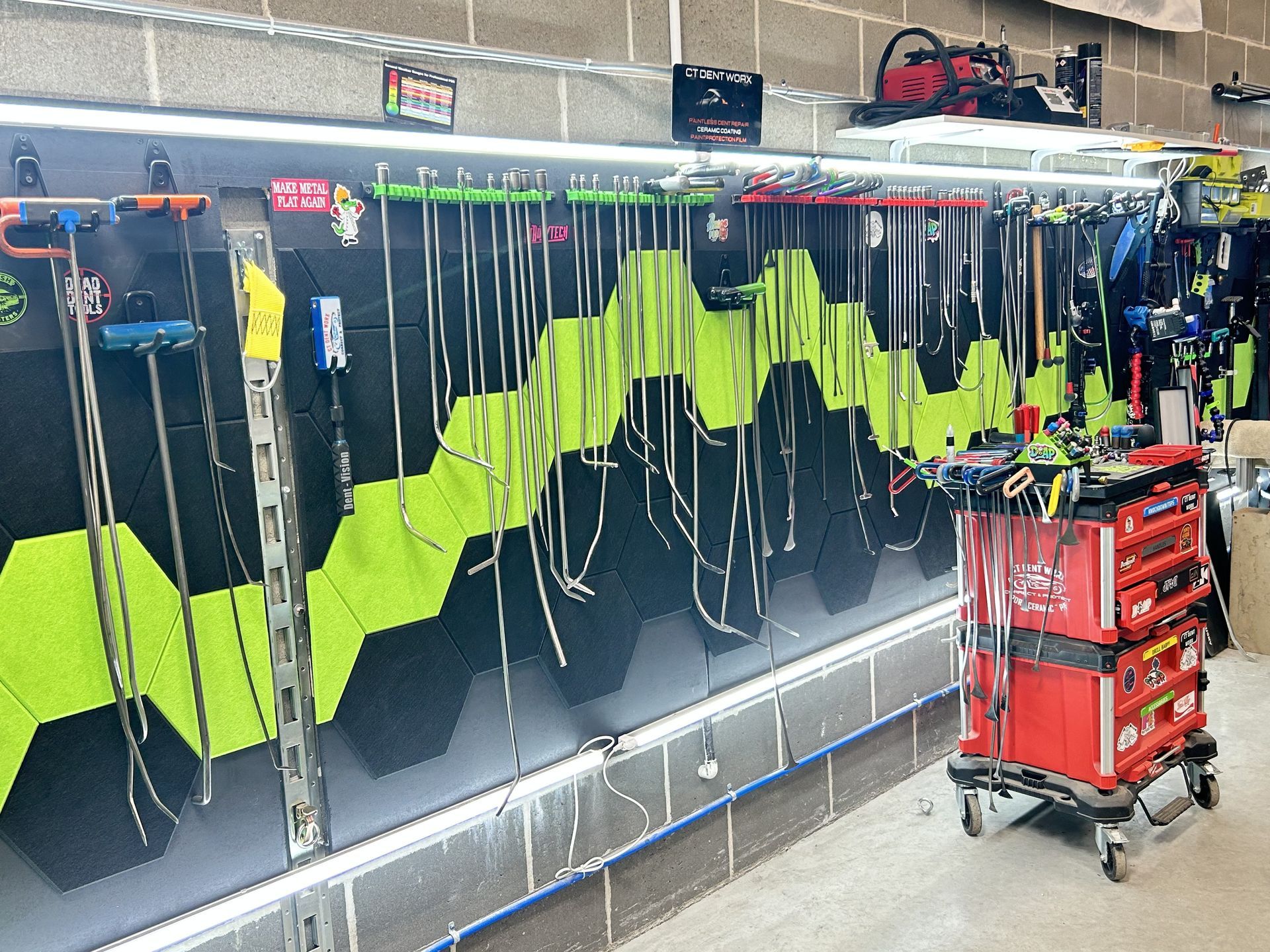 Rows of lime-green safety vests and tools hanging in a workshop, with a red rolling tool cart in front