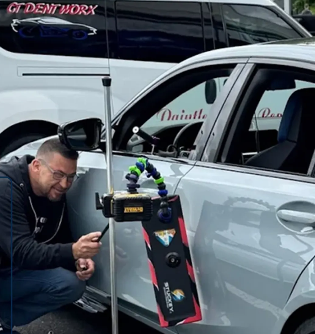 Man kneels beside a white car, inspecting a device mounted on the door in a garage.
