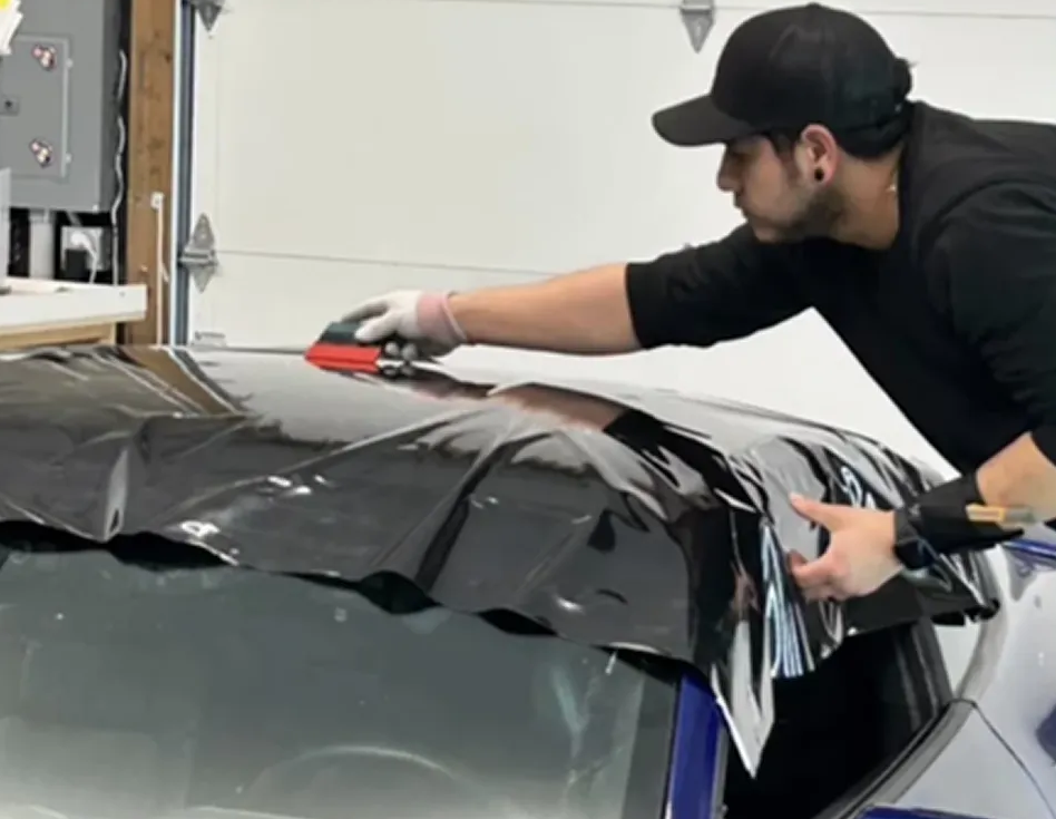Technician applying black vinyl wrap to a car roof in a workshop Technician applying black vinyl wrap to a car roof in a workshop