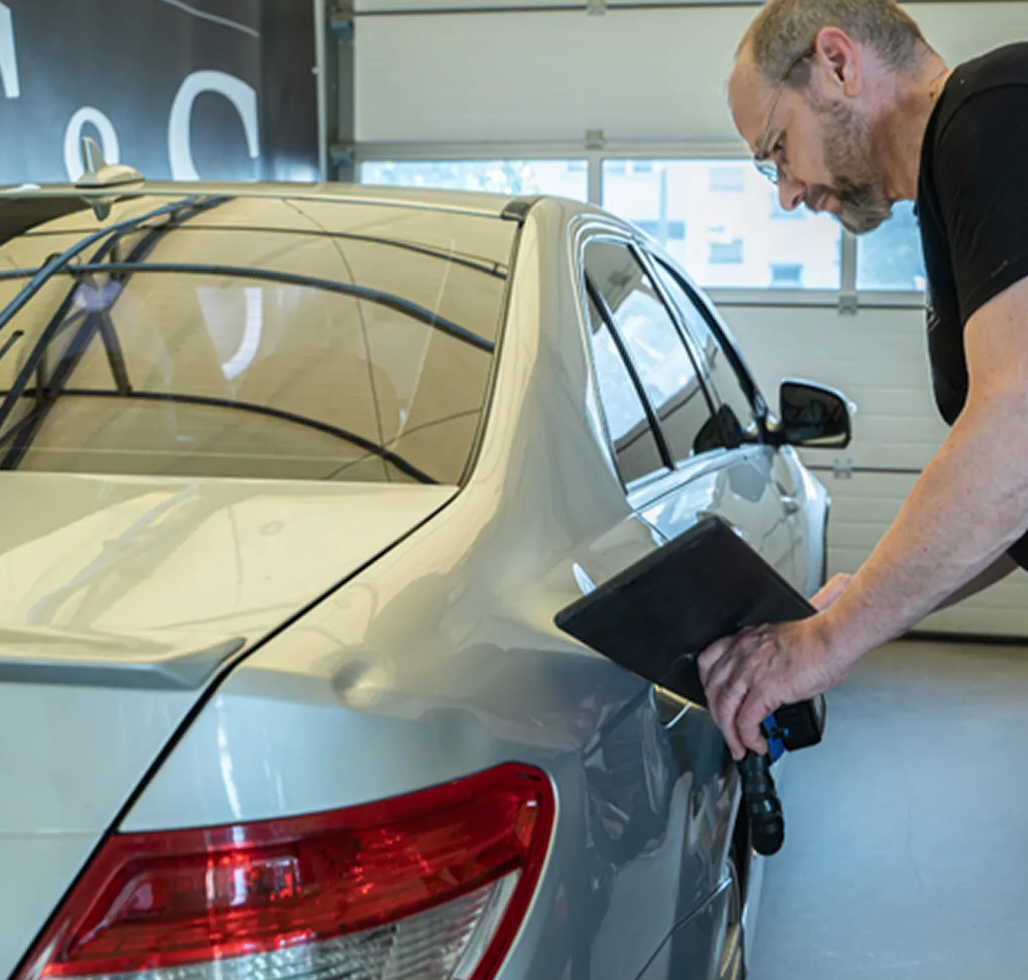 Man using a device to inspect a silver car in a garage workshop Man using a device to inspect a silver car in a garage workshop