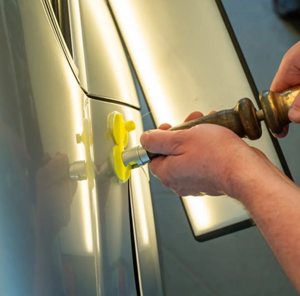 Hands using a suction-cup dent puller on a car door to remove a dent Hands using a suction-cup dent puller on a car door to remove a dent