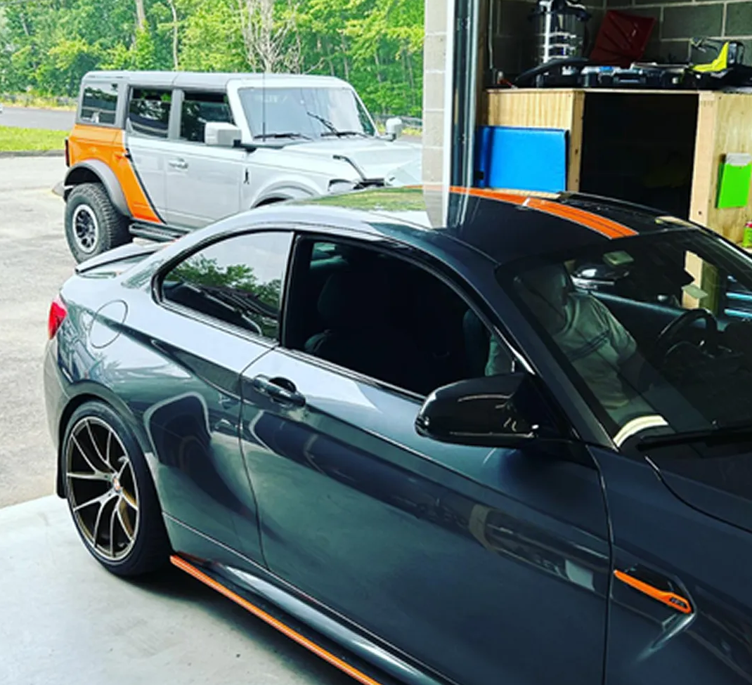 Dark blue sports coupe with orange accents parked in a garage, with a silver SUV in the background