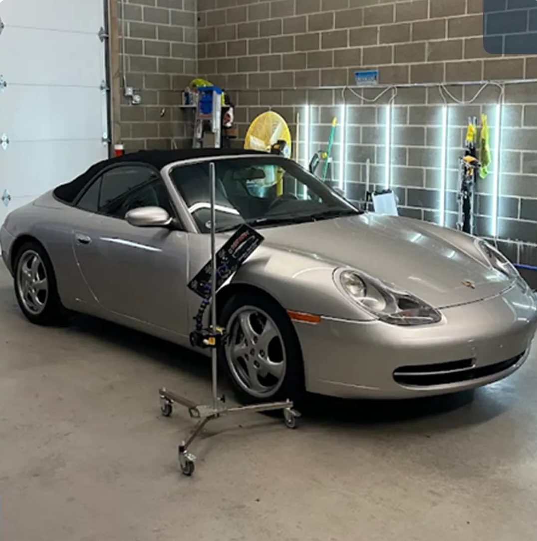 Silver convertible sports car in a garage, supported by a jack stand near the front wheel. Silver convertible sports car in a garage, supported by a jack stand near the front wheel.