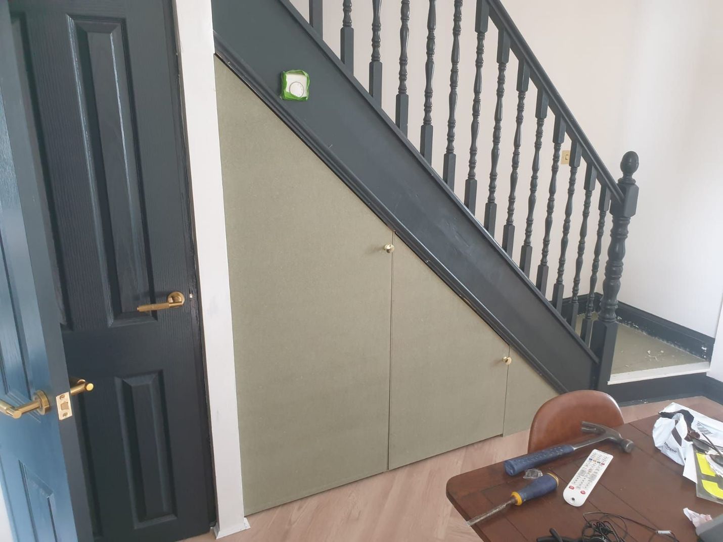 Storage built under stairs with dark blue door, black railing, and brass hardware.