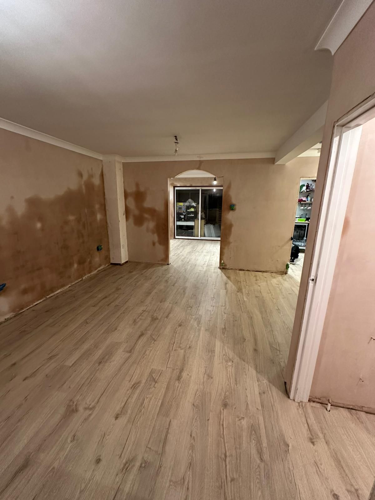 Interior of a room under renovation with new wood flooring and exposed plaster walls.