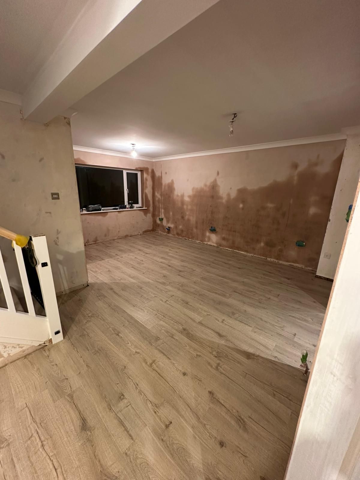 Interior room with unfinished walls and new wood flooring, a window, and a partial staircase.