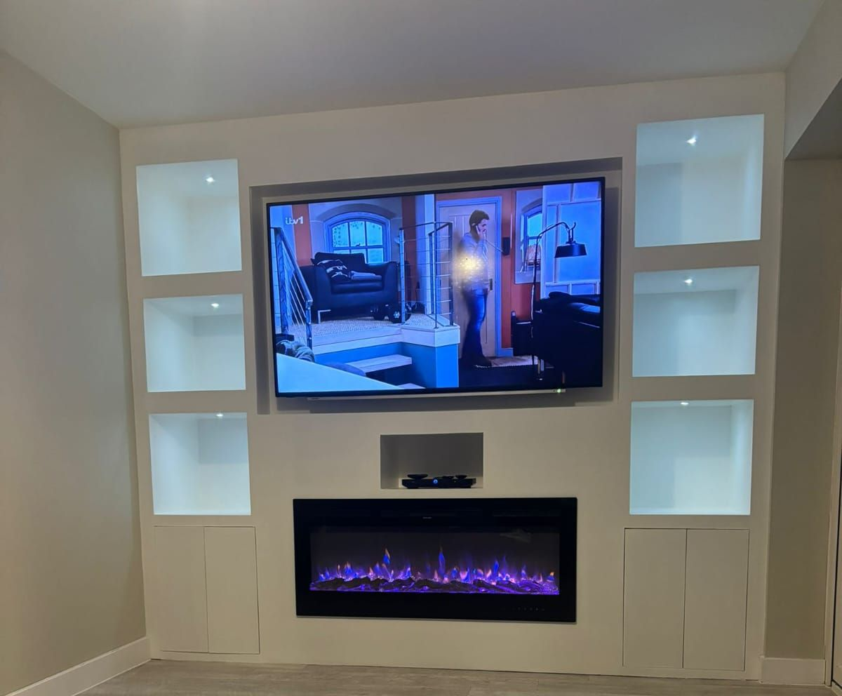 Built-in entertainment center with mounted TV, shelves, fireplace, and speaker on a beige wall.