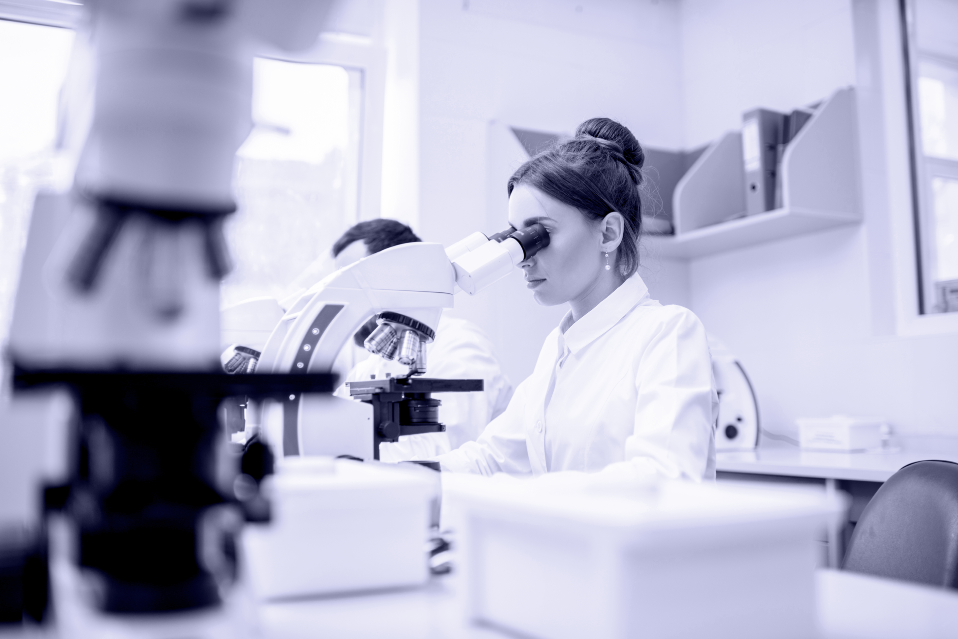 Woman in lab coat looking through a microscope in a laboratory setting.