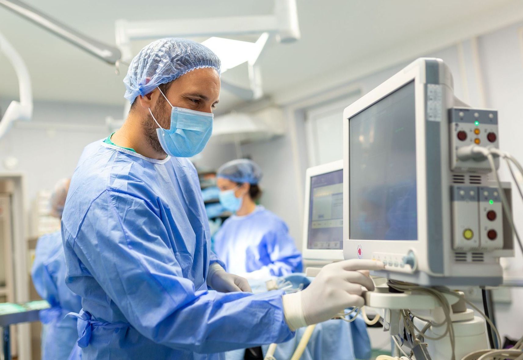 Surgeon in operating room, adjusting medical equipment, wearing mask and scrubs.