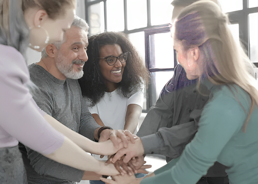 Group of people with hands stacked together, smiling in a bright room.